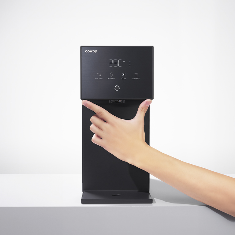 A hand reaching to the Coway Dazzie touch panel on a bright countertop
