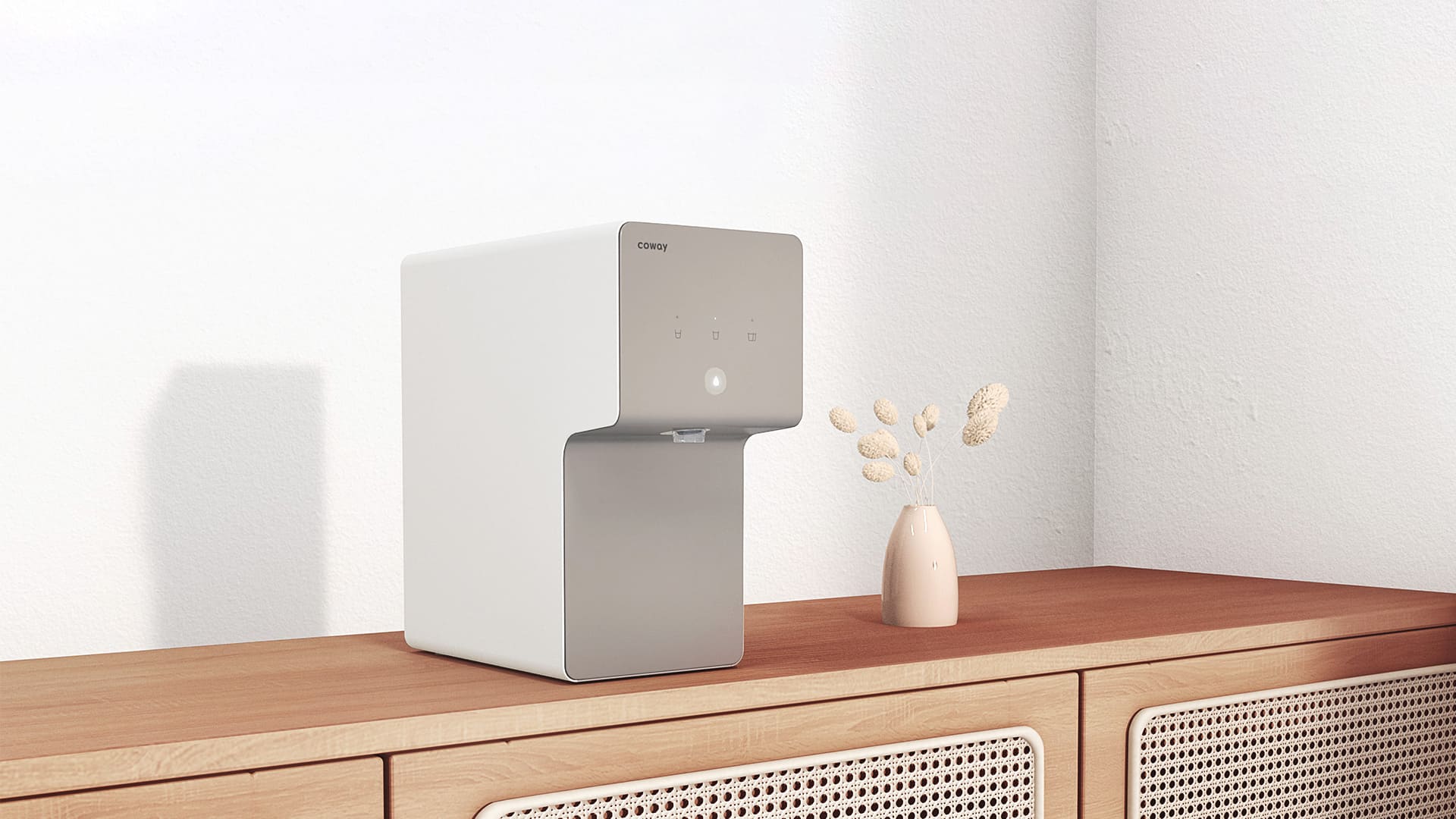Coway Cinnamon water purifier on a wooden cabinet beside a vase of dried flowers